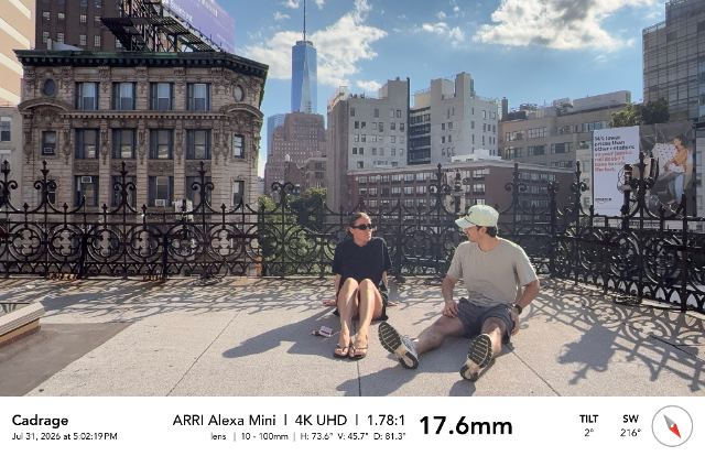 Cadrage location-scout frame: Roy and Hayley sitting on a Manhattan rooftop, One World Trade Center behind them, camera metadata bar along the bottom.